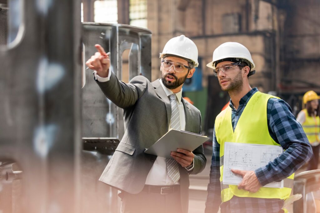 Manager and steel worker talking and looking away in factory